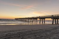 a sunset on a beach next to a pier in the sand with a horse drawn traces in the sand