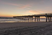 a sunset on a beach next to a pier in the sand with a horse drawn traces in the sand