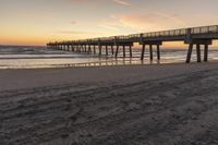 a sunset on a beach next to a pier in the sand with a horse drawn traces in the sand