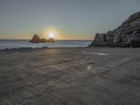 a lone motorcycle is parked near a rock formation on the beach at sunset, with water and ocean in the background