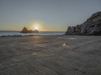 a lone motorcycle is parked near a rock formation on the beach at sunset, with water and ocean in the background