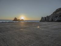 a lone motorcycle is parked near a rock formation on the beach at sunset, with water and ocean in the background