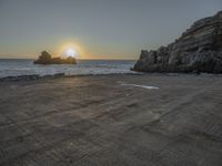 a lone motorcycle is parked near a rock formation on the beach at sunset, with water and ocean in the background