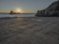 a lone motorcycle is parked near a rock formation on the beach at sunset, with water and ocean in the background