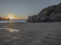 a lone motorcycle is parked near a rock formation on the beach at sunset, with water and ocean in the background