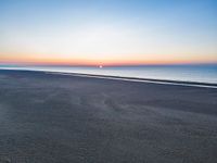 a lone person walks along an empty beach towards the water at sunset on a bright sunny day