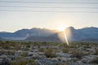 the sun is setting behind the mountains with bushes in foreground and power lines above