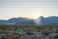 the sun is setting behind the mountains with bushes in foreground and power lines above