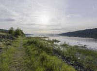 a bike rider rides along a path next to the river at sunset time in the distance