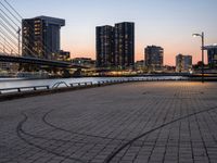 a man on a bike riding next to a river at sunset with the city lights of city buildings