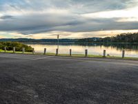 a bike parked in the parking lot next to the water at sunset time with clouds in background