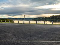 a bike parked in the parking lot next to the water at sunset time with clouds in background