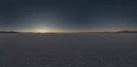 the sun sets over an empty, flat land with mountains in the background and the horizon as seen from a plane