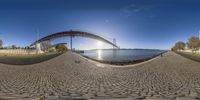 there is a fisheye lens that shows the bridge at sunset over water and an empty road to go under it