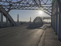 an empty road near the center of a bridge at sunset in a city setting in the sun, with buildings and other urban lights reflected in the distance