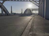 an empty road near the center of a bridge at sunset in a city setting in the sun, with buildings and other urban lights reflected in the distance