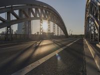 a road going under a bridge at sunset with the sun shining in the distance and buildings beyond