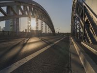 a road going under a bridge at sunset with the sun shining in the distance and buildings beyond