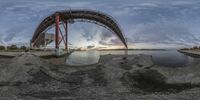 a panoramic shot of a bridge over the water at sunset on a cloudy day