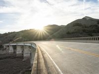 a highway and bridge crossing over the hillside side with the sun behind them at sunset