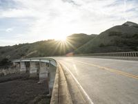 a highway and bridge crossing over the hillside side with the sun behind them at sunset