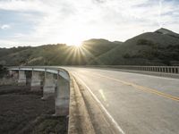 a highway and bridge crossing over the hillside side with the sun behind them at sunset