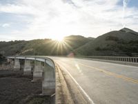 a highway and bridge crossing over the hillside side with the sun behind them at sunset