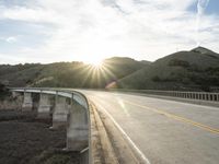 a highway and bridge crossing over the hillside side with the sun behind them at sunset