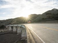 a highway and bridge crossing over the hillside side with the sun behind them at sunset