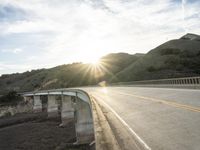 a highway and bridge crossing over the hillside side with the sun behind them at sunset