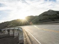 a highway and bridge crossing over the hillside side with the sun behind them at sunset