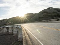 a highway and bridge crossing over the hillside side with the sun behind them at sunset