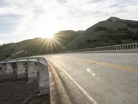 a highway and bridge crossing over the hillside side with the sun behind them at sunset