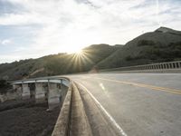 a highway and bridge crossing over the hillside side with the sun behind them at sunset