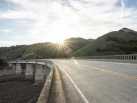 a highway and bridge crossing over the hillside side with the sun behind them at sunset