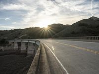 a highway and bridge crossing over the hillside side with the sun behind them at sunset