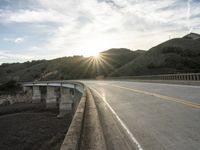 a highway and bridge crossing over the hillside side with the sun behind them at sunset