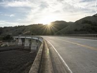 a highway and bridge crossing over the hillside side with the sun behind them at sunset