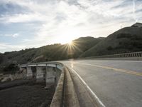 a highway and bridge crossing over the hillside side with the sun behind them at sunset