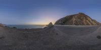 a very wide angle view of an almost empty mountain overlooking the water at sunset with the sun coming out