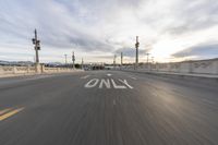 a sign that is on the street at sunset along a bridge with traffic signals in the distance