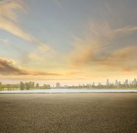 an empty parking lot with a city skyline in the distance during sunset or evening time