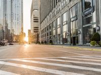 a paved city street surrounded by tall buildings in the sundown hour at sunset, with crosswalks and traffic