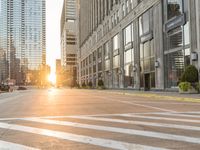 a paved city street surrounded by tall buildings in the sundown hour at sunset, with crosswalks and traffic