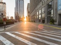 a paved city street surrounded by tall buildings in the sundown hour at sunset, with crosswalks and traffic