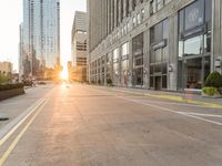 a paved city street surrounded by tall buildings in the sundown hour at sunset, with crosswalks and traffic