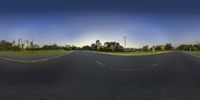 a wide angle photograph shows a road in the sunset with a city in the distance