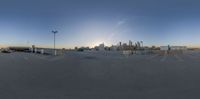 a parking lot with several cars in it, with buildings behind it at sunset in the background