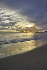 a beach during the sun setting in the background with people walking along it at the shore