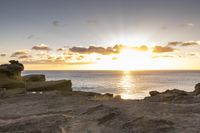 this person is on top of the cliff looking at the ocean and the sun going down